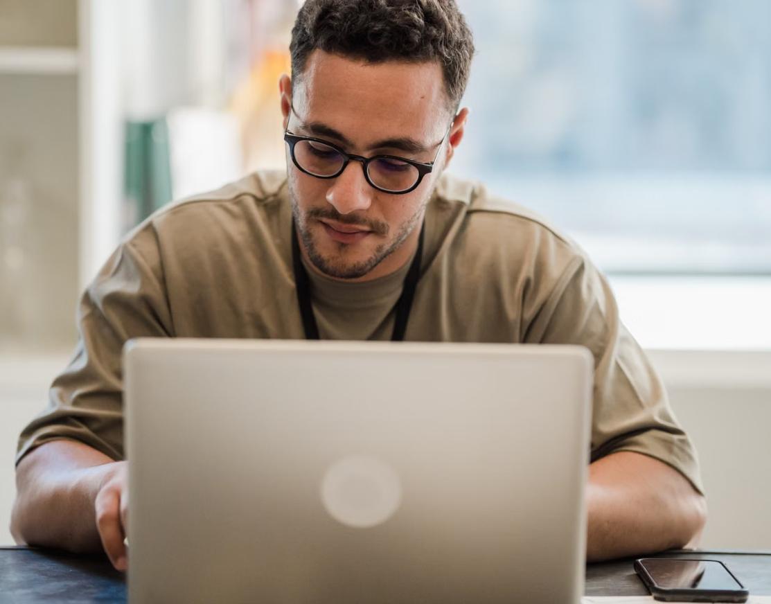 A person working focused on a laptop at a home desk near a window.