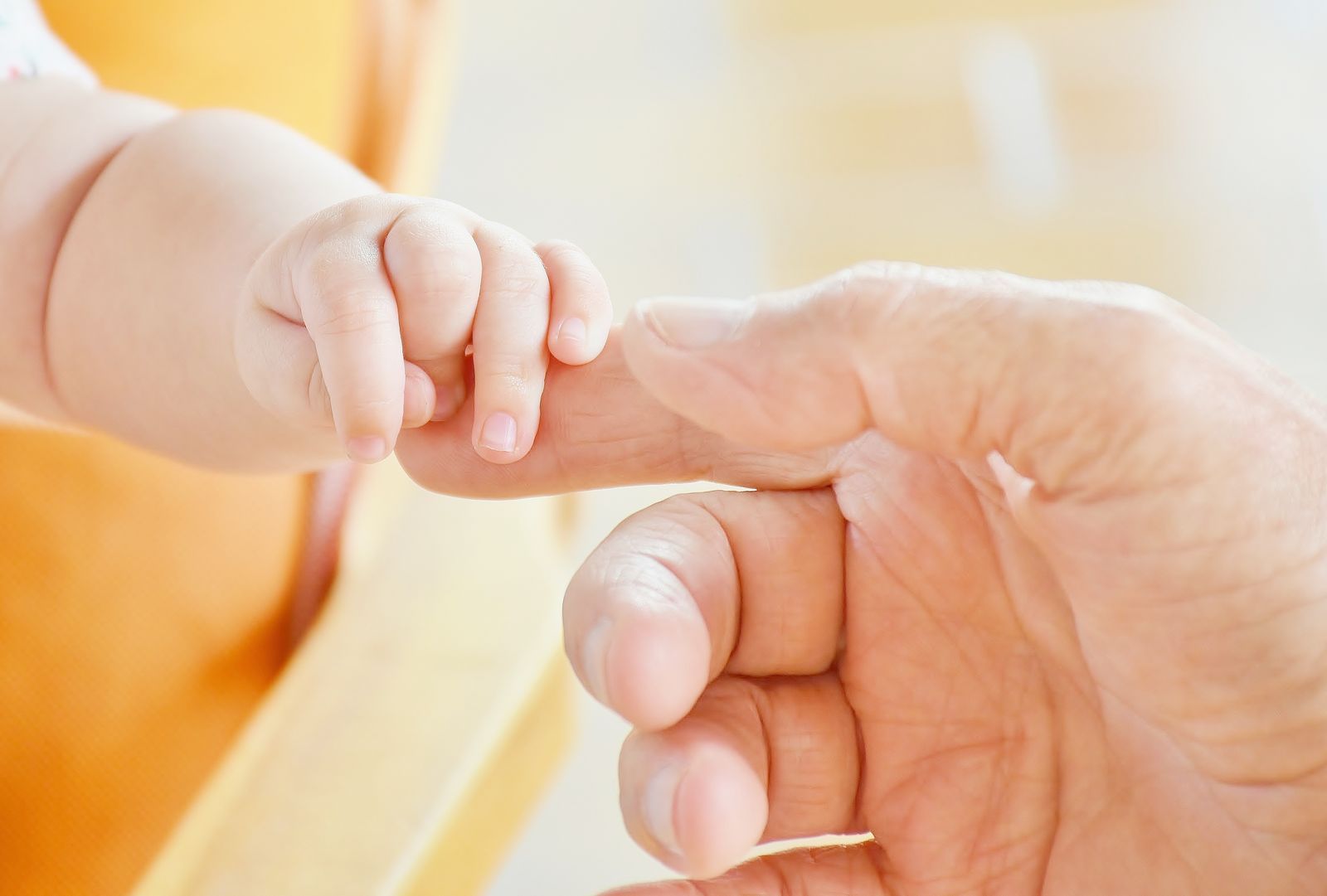 Close-up of a newborn baby's hand gripping an adult's finger against a soft warm background
