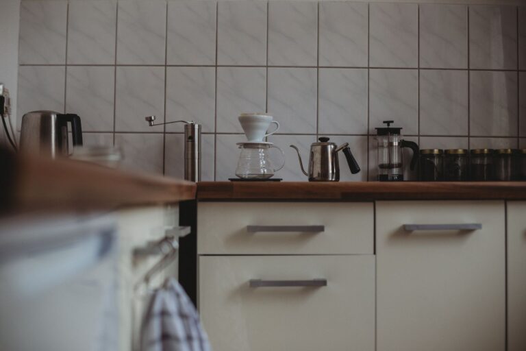 Kitchen counter with a pour-over dripper and glass carafe, hand coffee grinder, gooseneck kettle and French press against white tiles